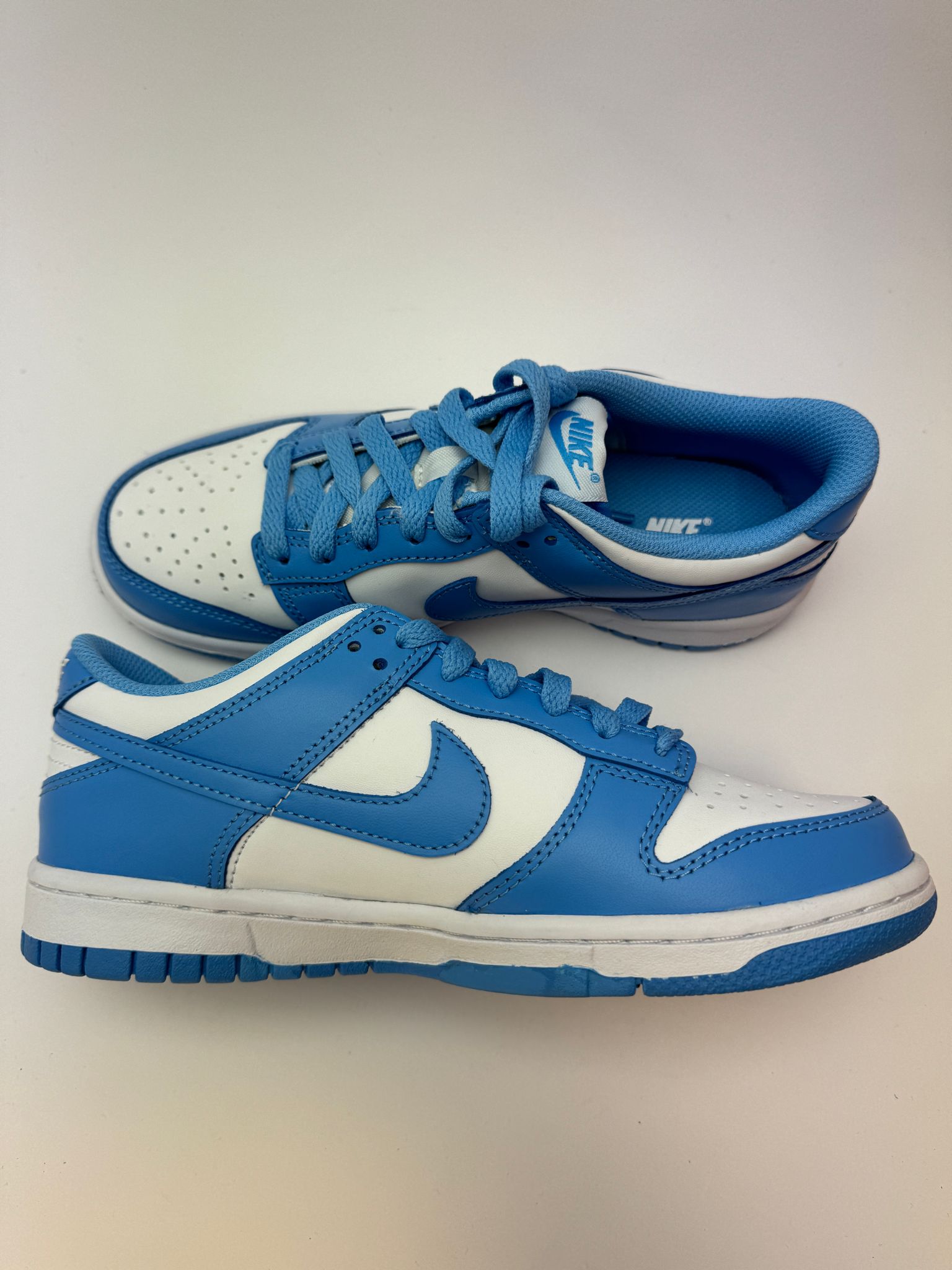 Nike Dunk Low UNC – linke Außenseite mit grauem Swoosh und typischem Helvetica-Branding unter dem Logo