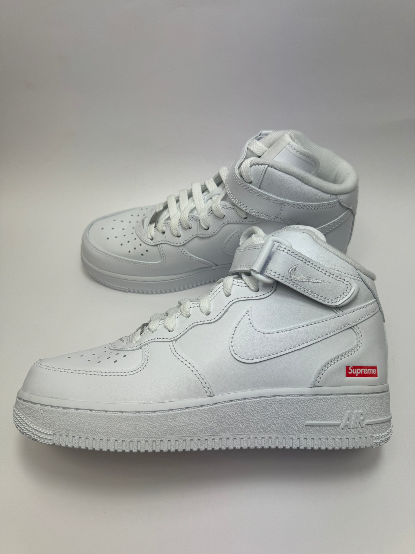 Seitenansicht des Nike Air Force 1 Mid Supreme White mit cleanem All-White Leder-Upper und Strap-Detail